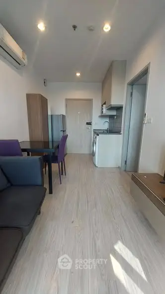 Modern apartment interior with open kitchen and dining area, featuring sleek furniture and bright lighting.