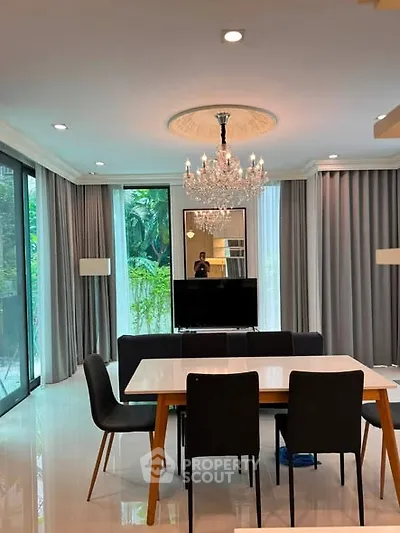 Elegant dining area with chandelier and garden view, featuring modern furniture and floor-to-ceiling windows.