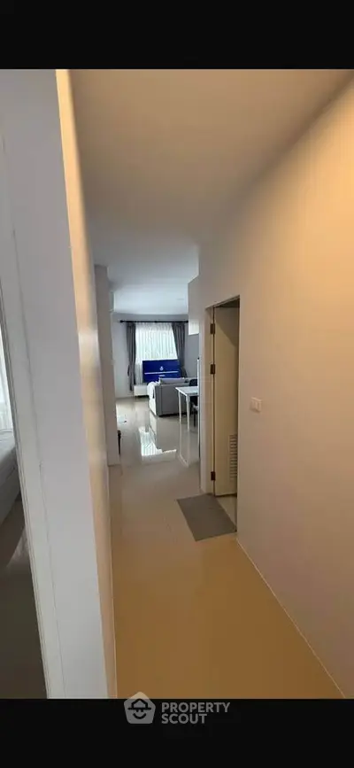 Modern apartment hallway leading to a bright living room with large windows and sleek furnishings.