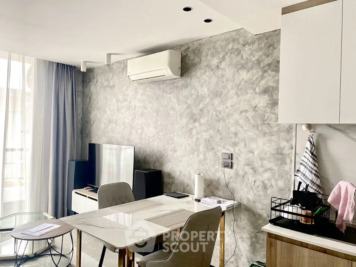 Modern living room with stylish decor and open kitchen layout, featuring air conditioning and natural light.