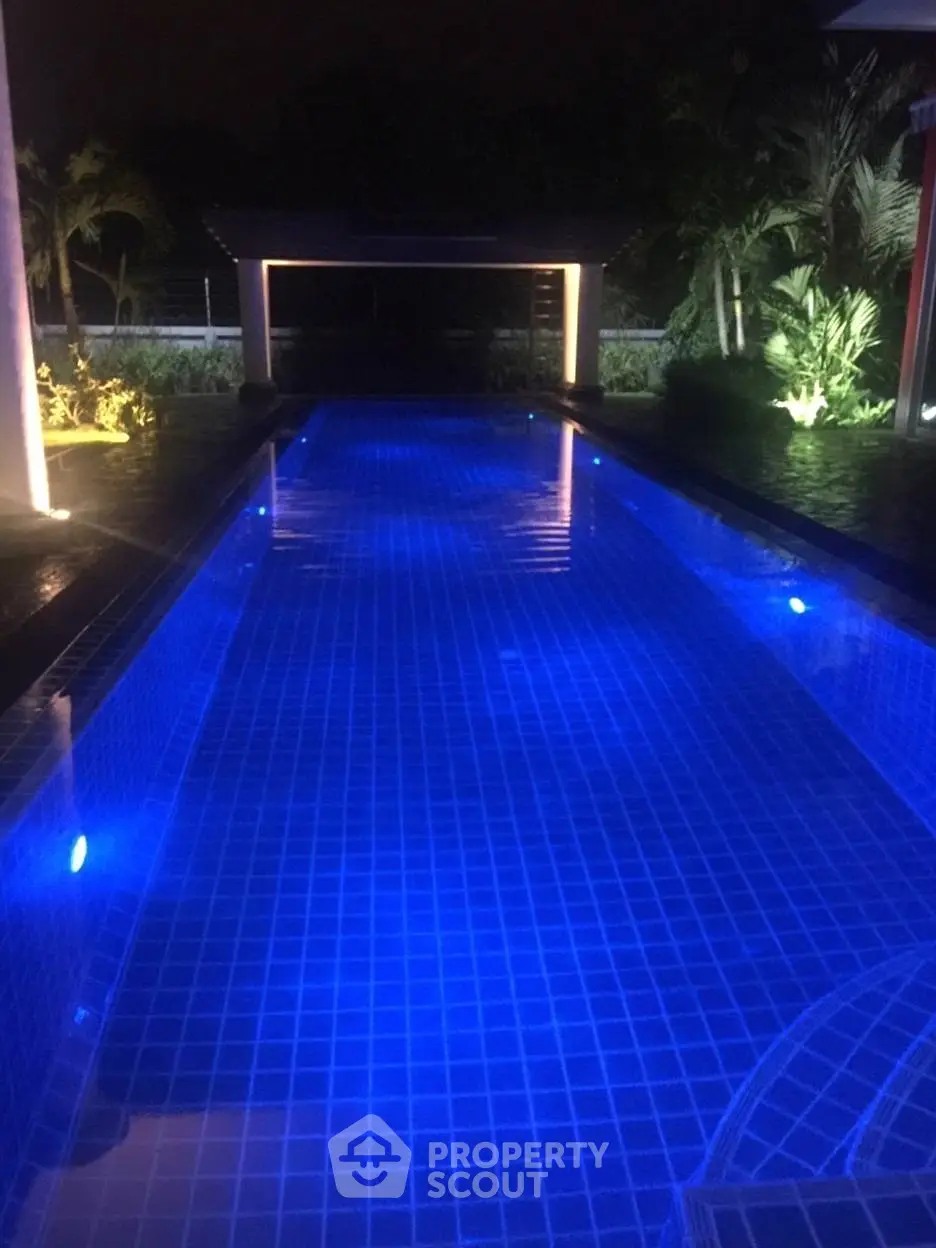 Luxurious illuminated swimming pool with serene night ambiance and lush greenery, perfect for relaxation.