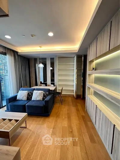 Modern living room with wooden flooring and built-in shelves, featuring a cozy blue sofa and elegant dining area.