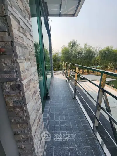 Modern balcony with glass railing and stone wall, offering a serene garden view.