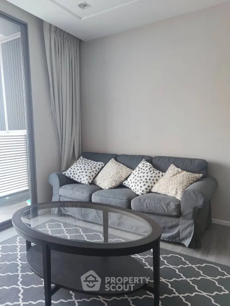 Elegant living room with plush grey sofa adorned with patterned cushions, sleek glass-top coffee table, and chic grey patterned rug, offering a serene urban retreat.