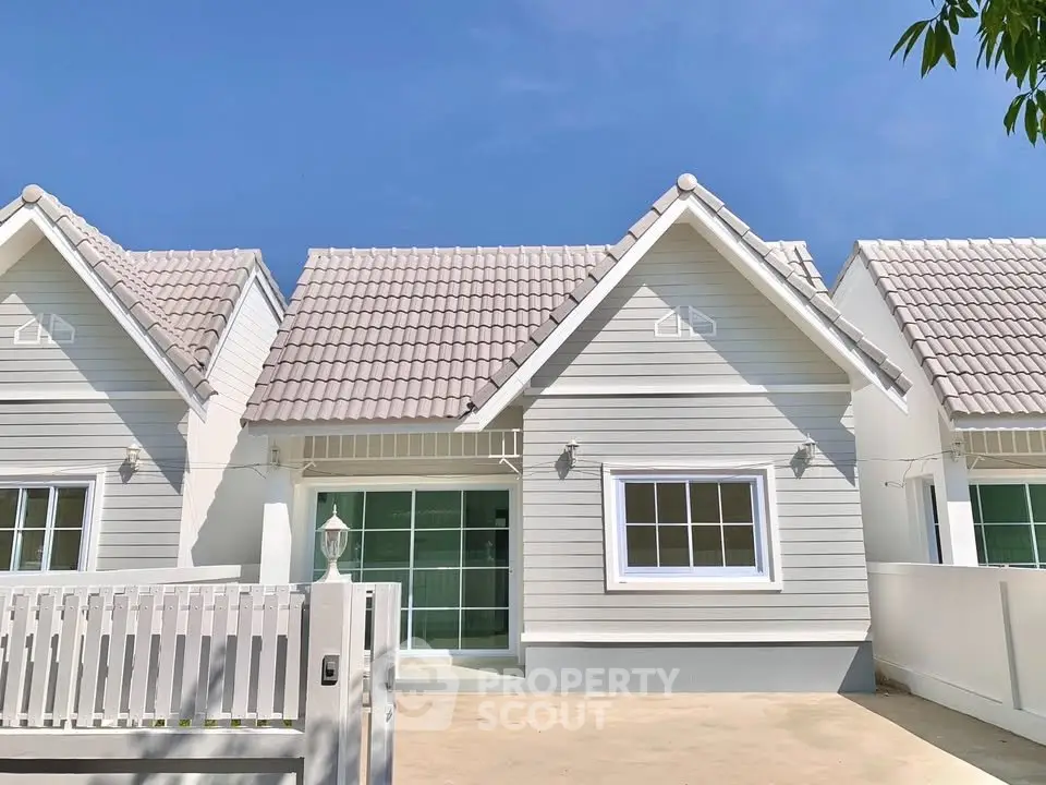 Charming suburban house with white picket fence and modern design under clear blue sky.