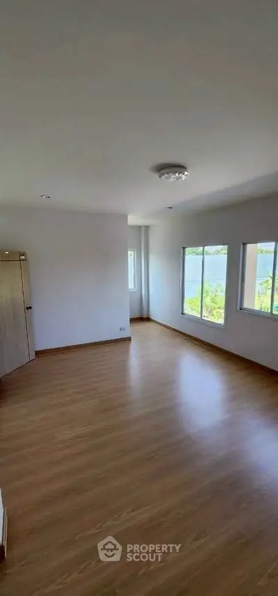 Spacious empty room with wooden flooring and large windows for natural light