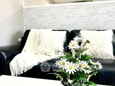 Chic living room with black leather sofa, white brick wall, and floral decor for modern elegance.