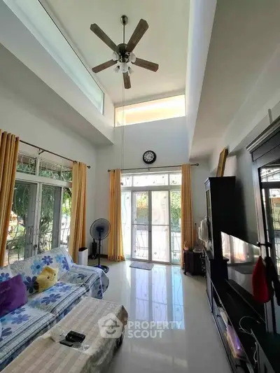 Spacious living room with high ceiling and large windows, featuring modern decor and natural light.