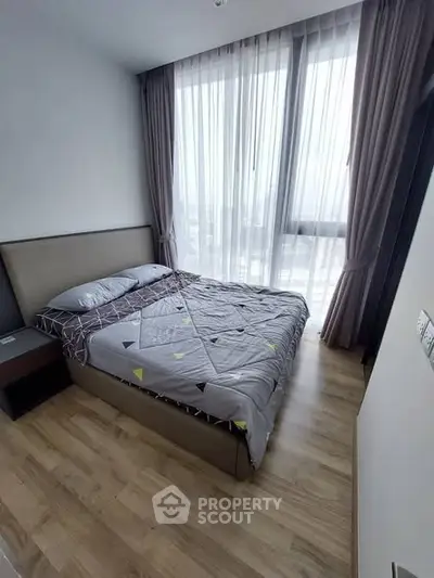 Cozy bedroom with modern decor and large window offering natural light.