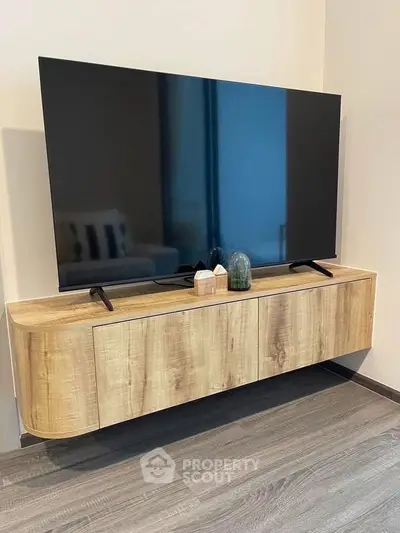 Modern living room with sleek wooden TV stand and large flat-screen TV, showcasing contemporary interior design.