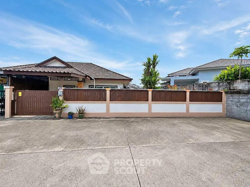 Charming suburban house with spacious driveway and modern fence under clear blue sky.