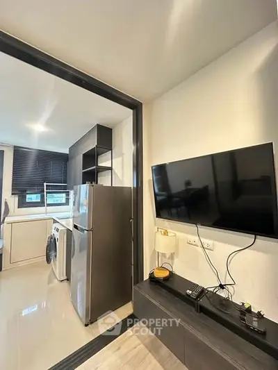 Modern kitchen with stainless steel appliances and wall-mounted TV in sleek apartment.