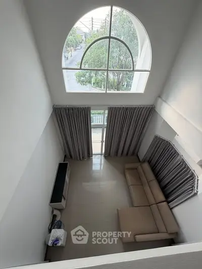 Spacious living room with high ceiling and large arched window offering a stunning view.
