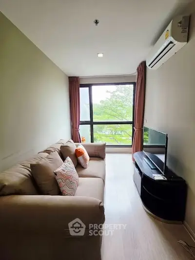 Cozy living room with large window and modern furnishings, offering a serene view of greenery.