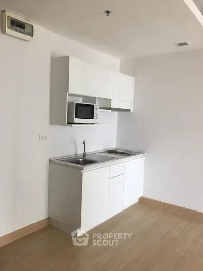 Modern minimalist kitchen with white cabinetry and microwave in sleek apartment
