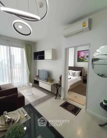 Modern living room with stylish decor and adjacent bedroom, featuring contemporary lighting and sleek furniture.