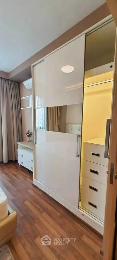 Modern bedroom with sleek wardrobe and wooden flooring, featuring elegant curtains and stylish decor.