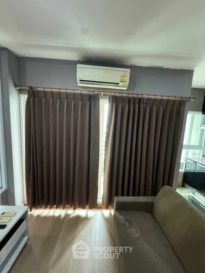 Cozy living room with air conditioning and large window draped with elegant curtains.
