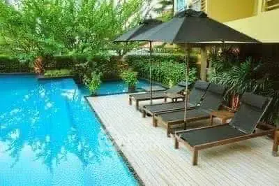 Luxurious poolside area with sun loungers and umbrellas in a serene garden setting.