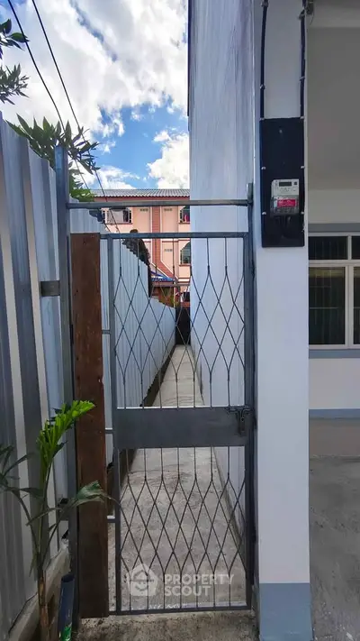 Narrow alleyway entrance with metal gate leading to residential building under clear blue sky.