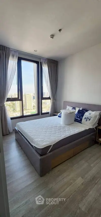 Bright bedroom with large window offering city view, featuring a cozy bed and modern decor.