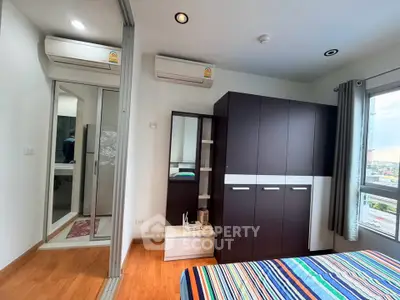 Modern bedroom with large wardrobe and air conditioning, featuring wooden flooring and colorful bedding.