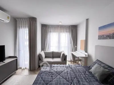 Modern bedroom with cozy sofa and study area, featuring large windows and elegant decor.