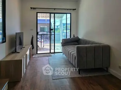 Modern living room with stylish sofa and TV, leading to a balcony with natural light.