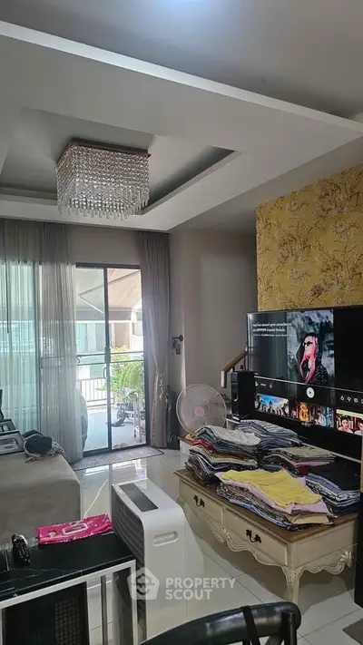Spacious living room with elegant chandelier and balcony access, featuring modern decor and entertainment setup.