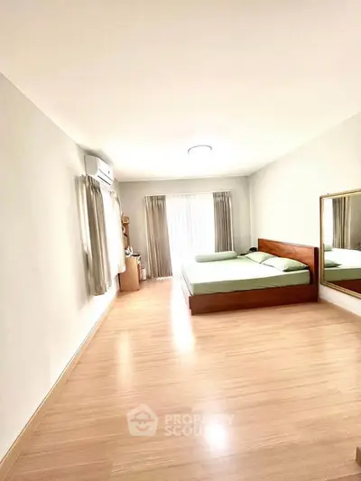 Spacious bedroom with wooden flooring and large mirror, featuring a comfortable bed and natural light.