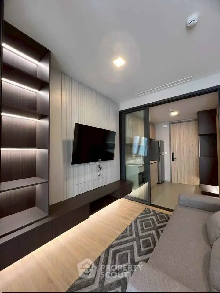Modern living room with sleek shelving and wall-mounted TV, leading to a stylish kitchen area.