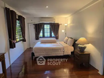 Cozy bedroom with wooden floors, stylish lamps, and large windows offering natural light.