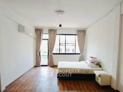 Spacious bedroom with wooden flooring and large windows for natural light.