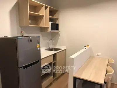Modern compact kitchen with fridge, microwave, and dining area in cozy apartment.