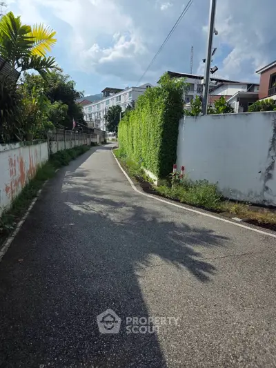 Charming residential street with lush greenery and modern apartment buildings under a clear blue sky.