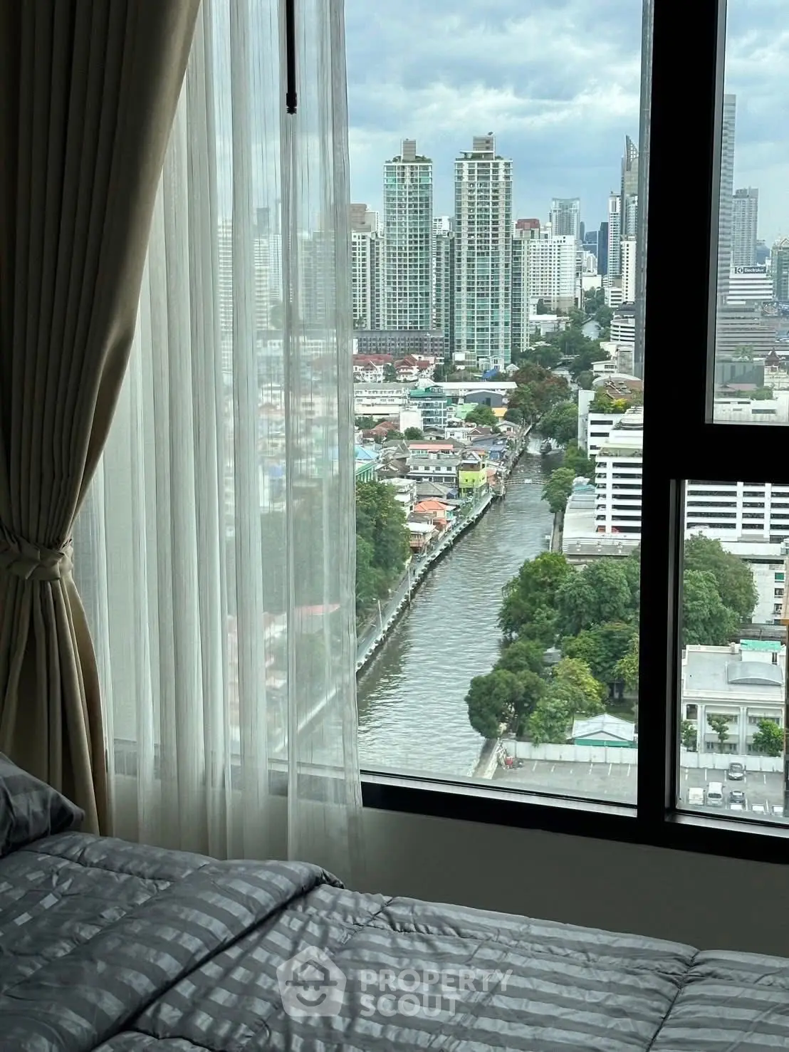 Stunning city view from a modern bedroom window with luxurious curtains and bedding.
