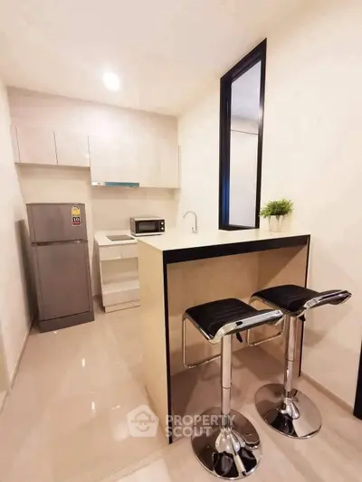 Modern kitchen with sleek bar stools and compact appliances in a stylish apartment.