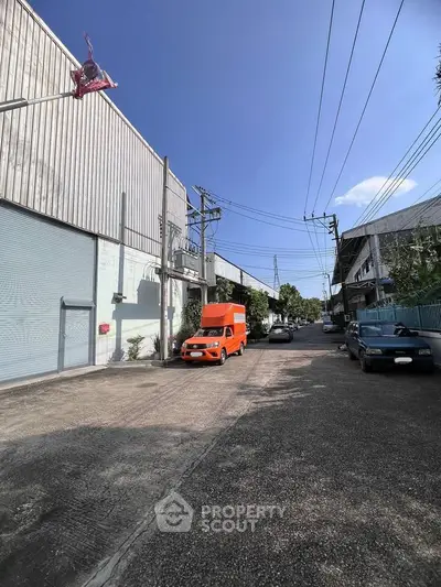 Industrial warehouse exterior with parking area and street view under clear blue sky.