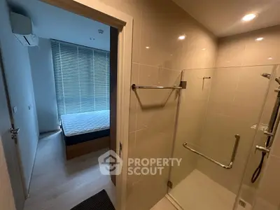 Modern bathroom with glass shower and view into bedroom with natural light.