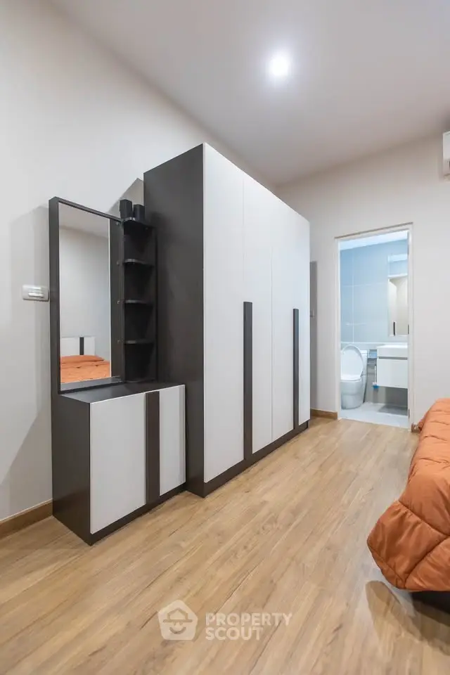 Modern bedroom with sleek wardrobe and ensuite bathroom, featuring warm wooden flooring and contemporary design.
