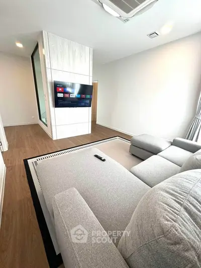 Modern living room with sleek design and large sectional sofa, featuring a wall-mounted TV and elegant wood flooring.