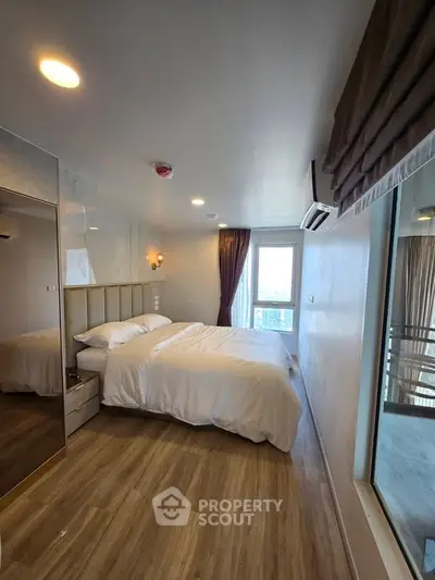 Modern bedroom with wooden flooring and large window offering natural light