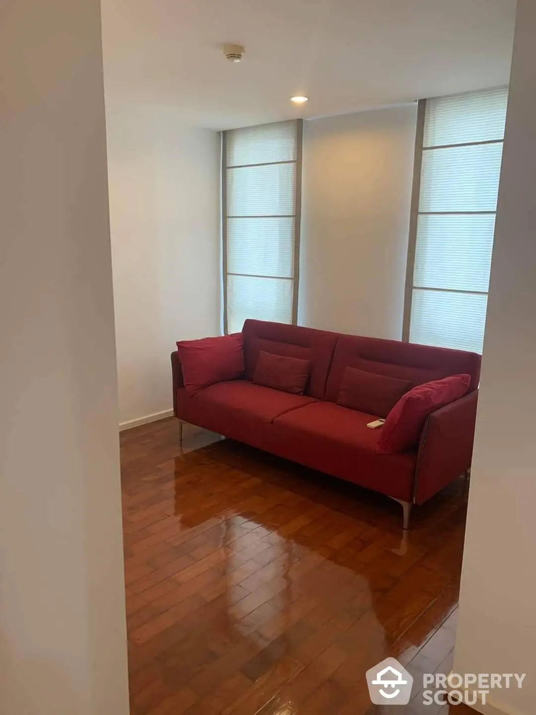 Spacious and well-lit living room with polished hardwood floors and a vibrant red sofa, offering a comfortable and stylish living space.