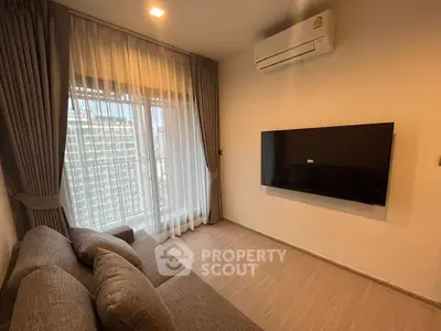 Modern living room with cozy sofa and wall-mounted TV, featuring large window with city view.