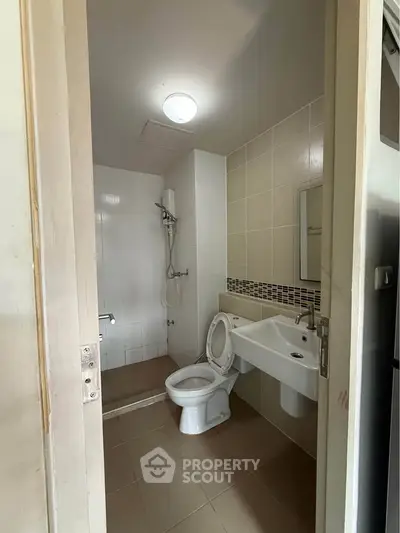 Compact bathroom with shower, toilet, and sink in modern apartment.