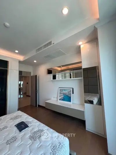 Modern bedroom with stylish decor and wooden flooring, featuring a large mirror and elegant lighting.
