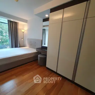 Modern bedroom with wooden flooring and large wardrobe, featuring natural light from window.