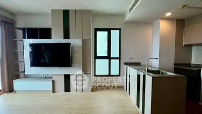 Modern living room with sleek TV unit and compact kitchen area in open layout apartment.
