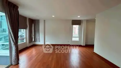 Spacious empty room with wooden flooring and large windows in modern apartment.