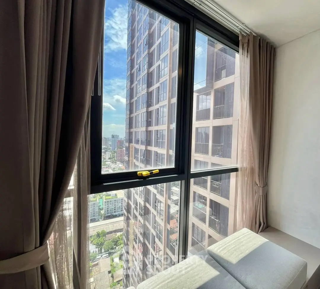 Stunning city view from modern high-rise apartment window with elegant curtains and bright natural light.